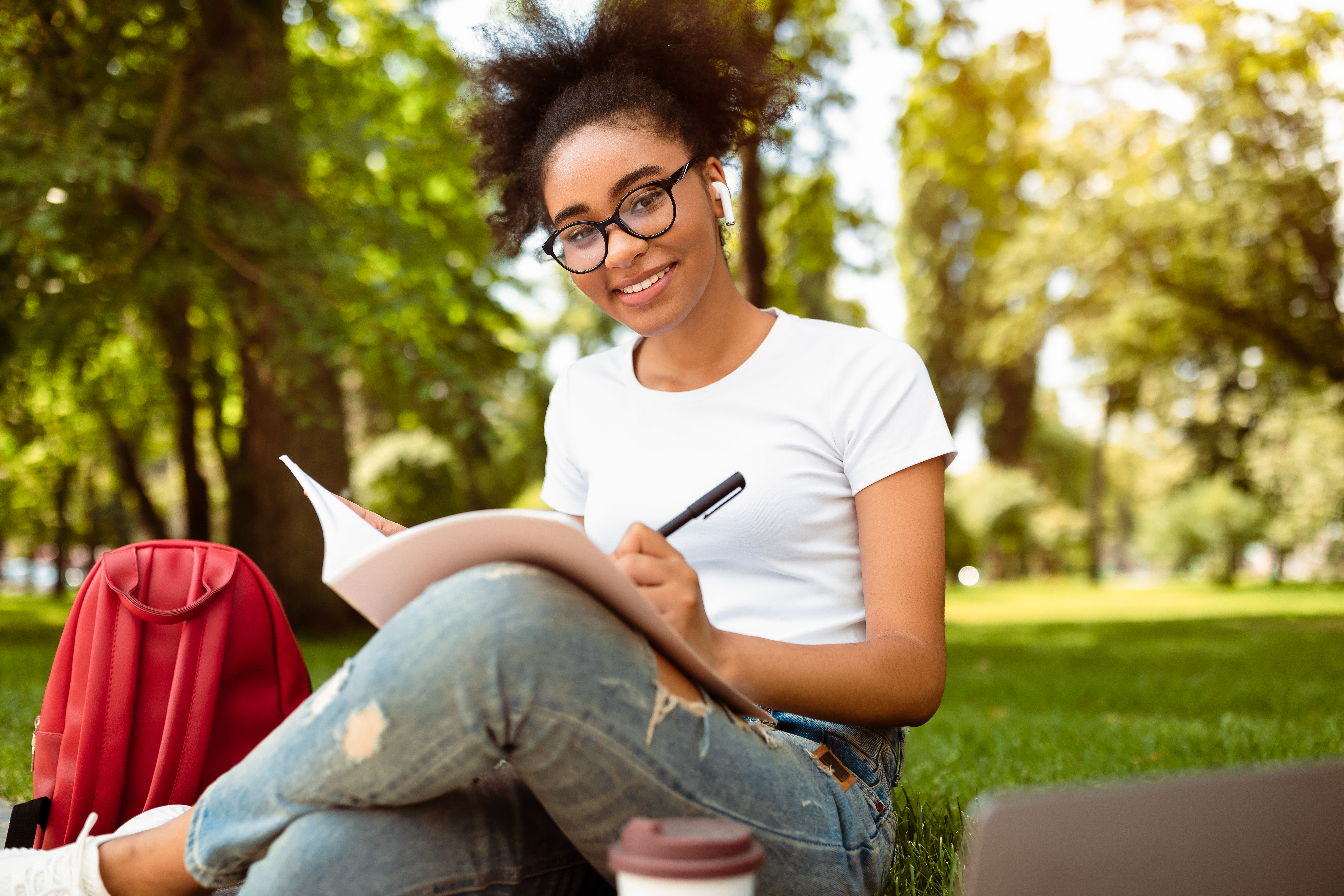 Cheerful Black College Girl Taking Notes Learning Sitting In Park Young women laughing together