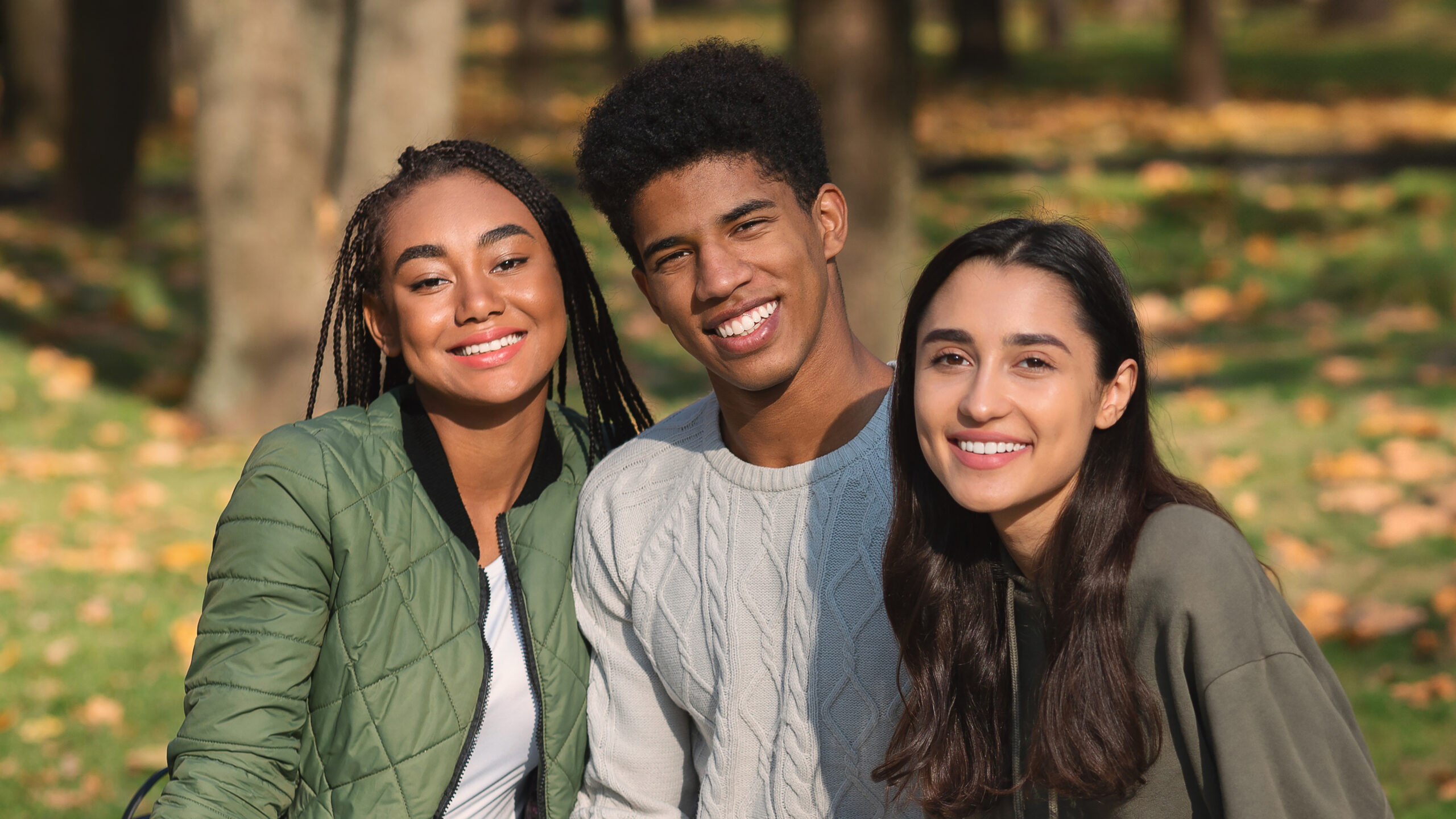 Cheerful teen friends sitting on bench with gadgets Smiling young woman